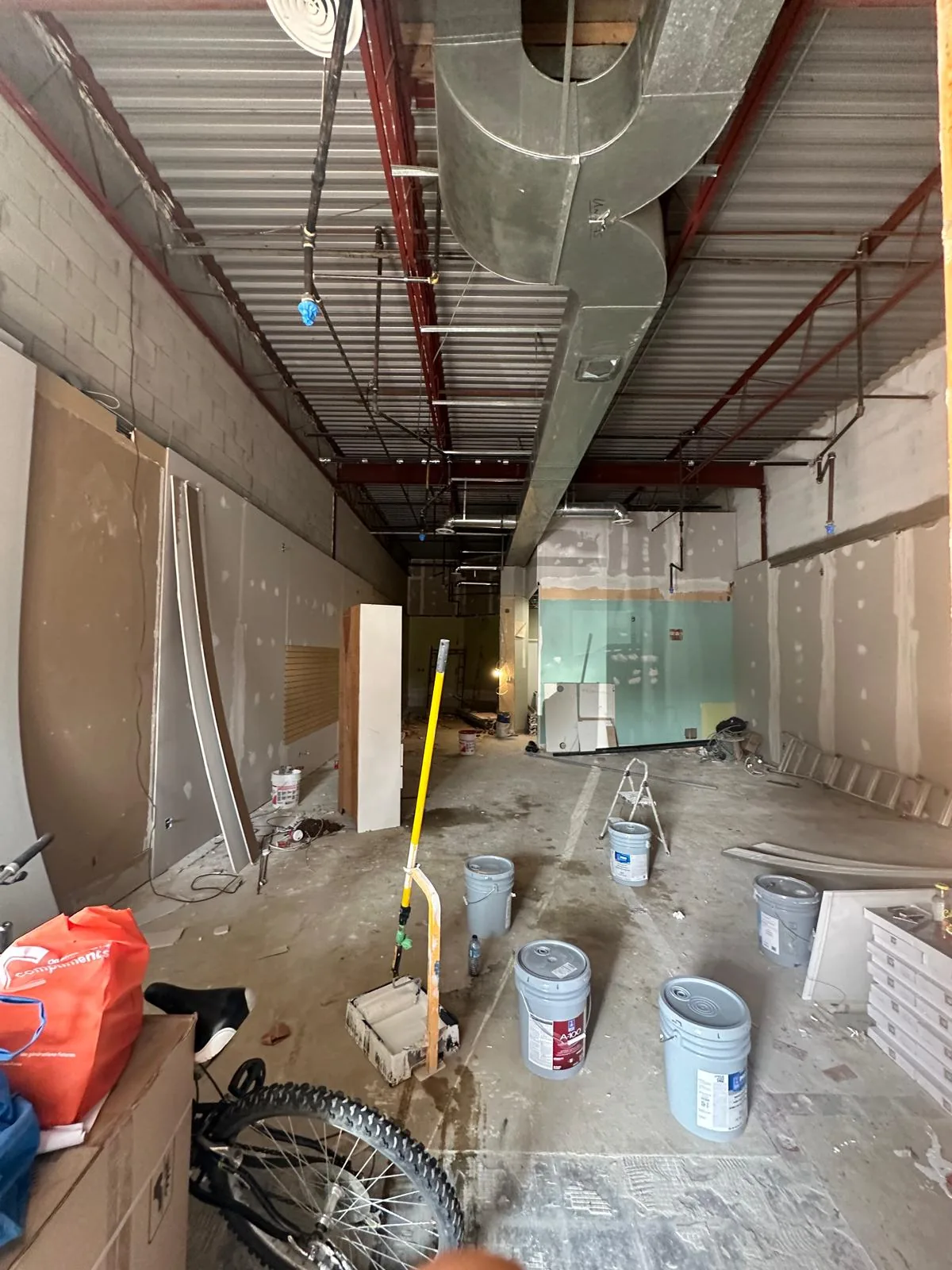 The former office unit stripped to its shell, with exposed ductwork, steel deck, old drywall and paint pails on a bare concrete floor