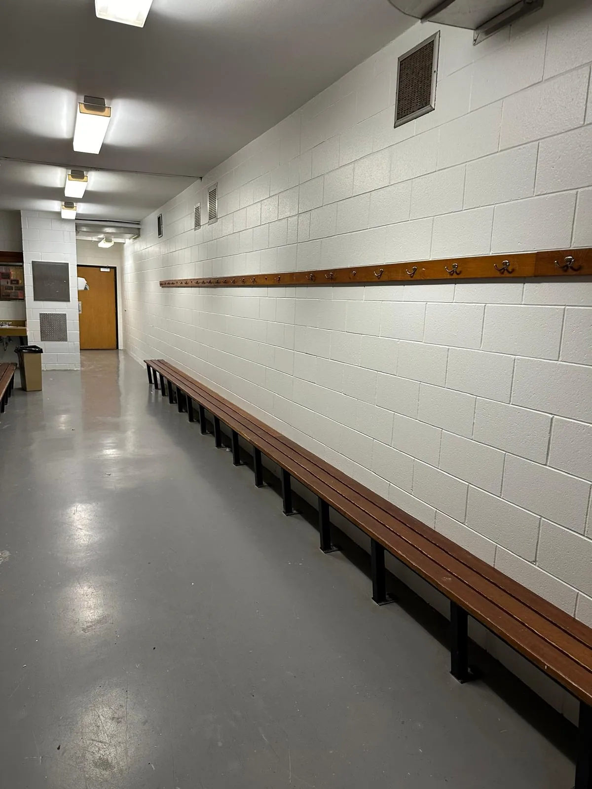A change room with block walls repainted in a washable white finish above a long wooden bench