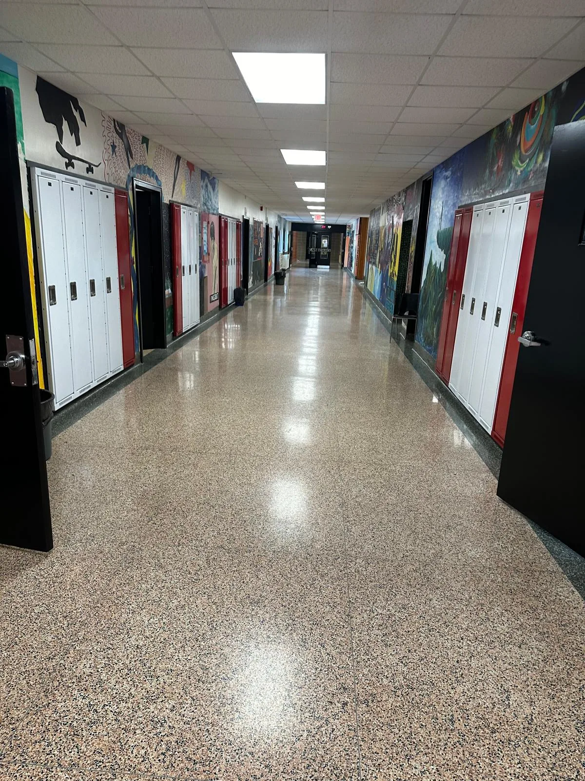 A long school corridor lined with lockers and student murals, with black-finished door frames