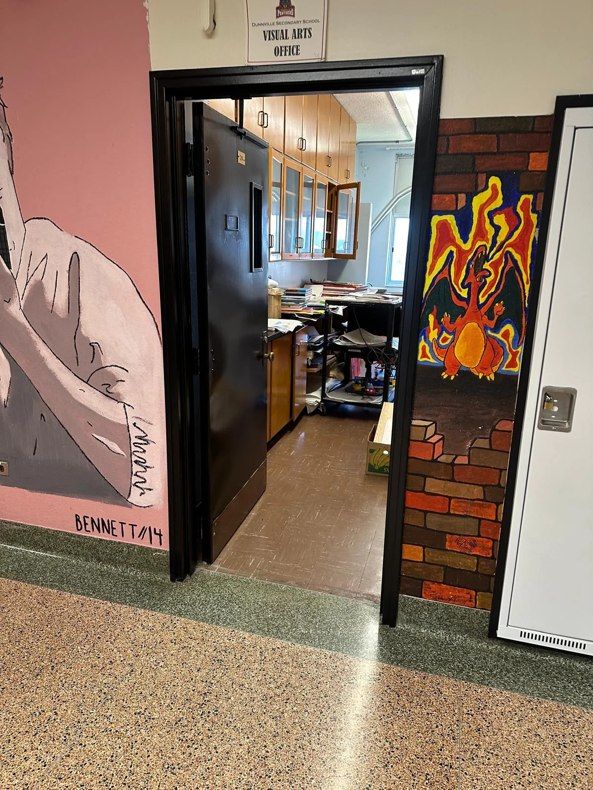The visual arts office door and frame finished in black, between student murals