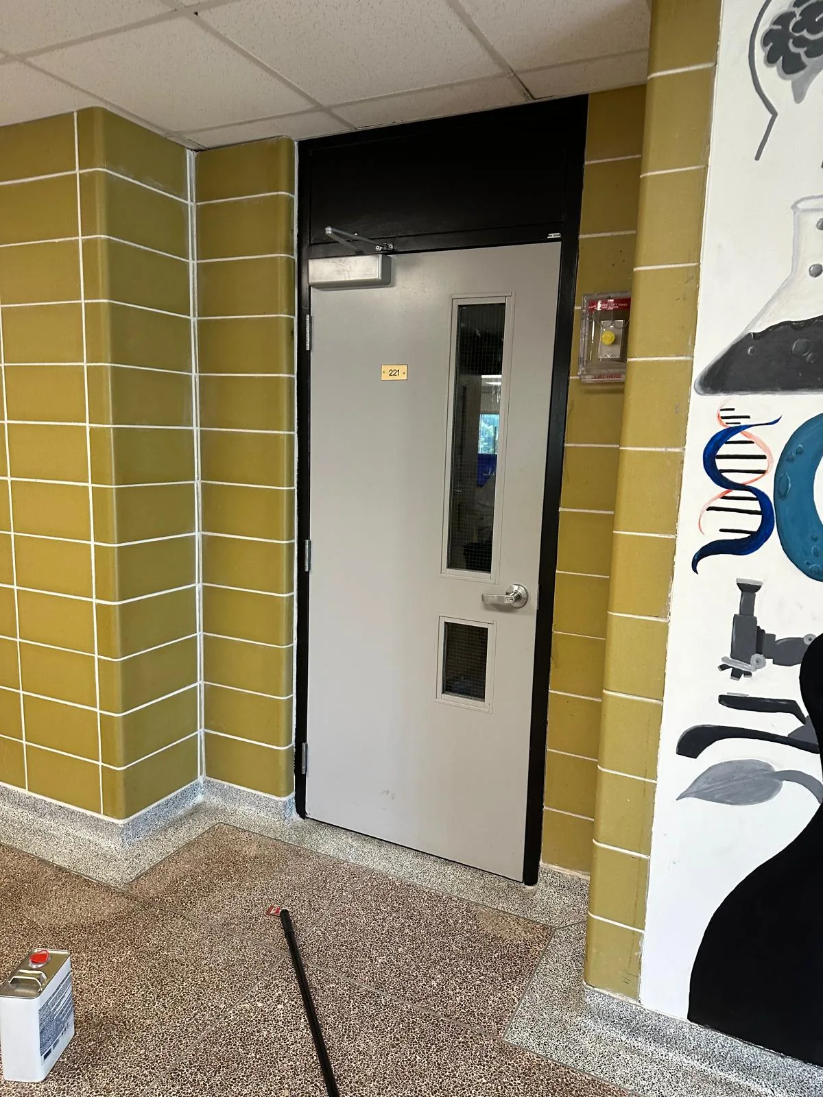 A classroom door in light grey set in a frame and transom panel freshly finished in black