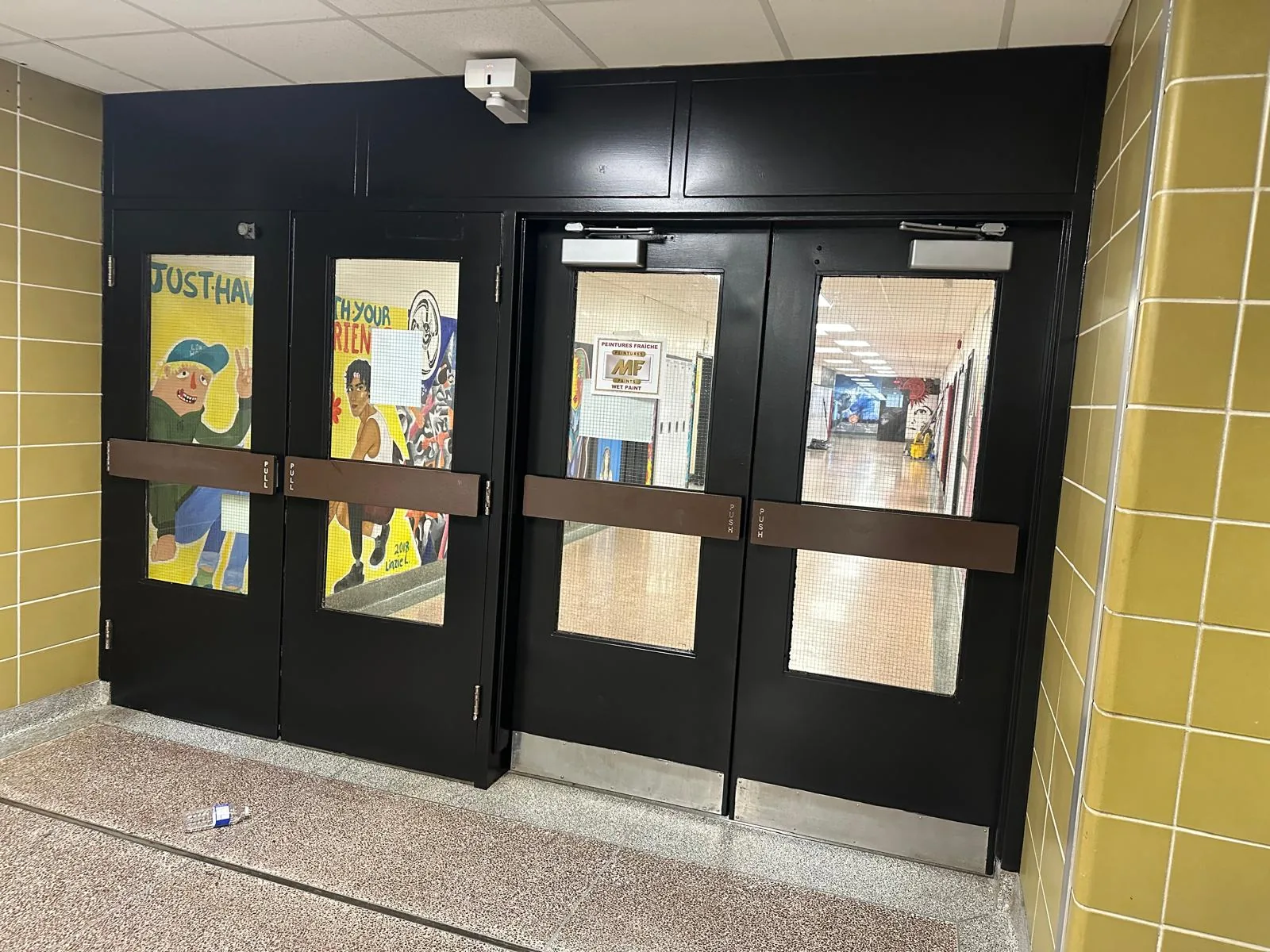 A bank of four corridor doors and their frames finished in black enamel between yellow glazed-tile walls
