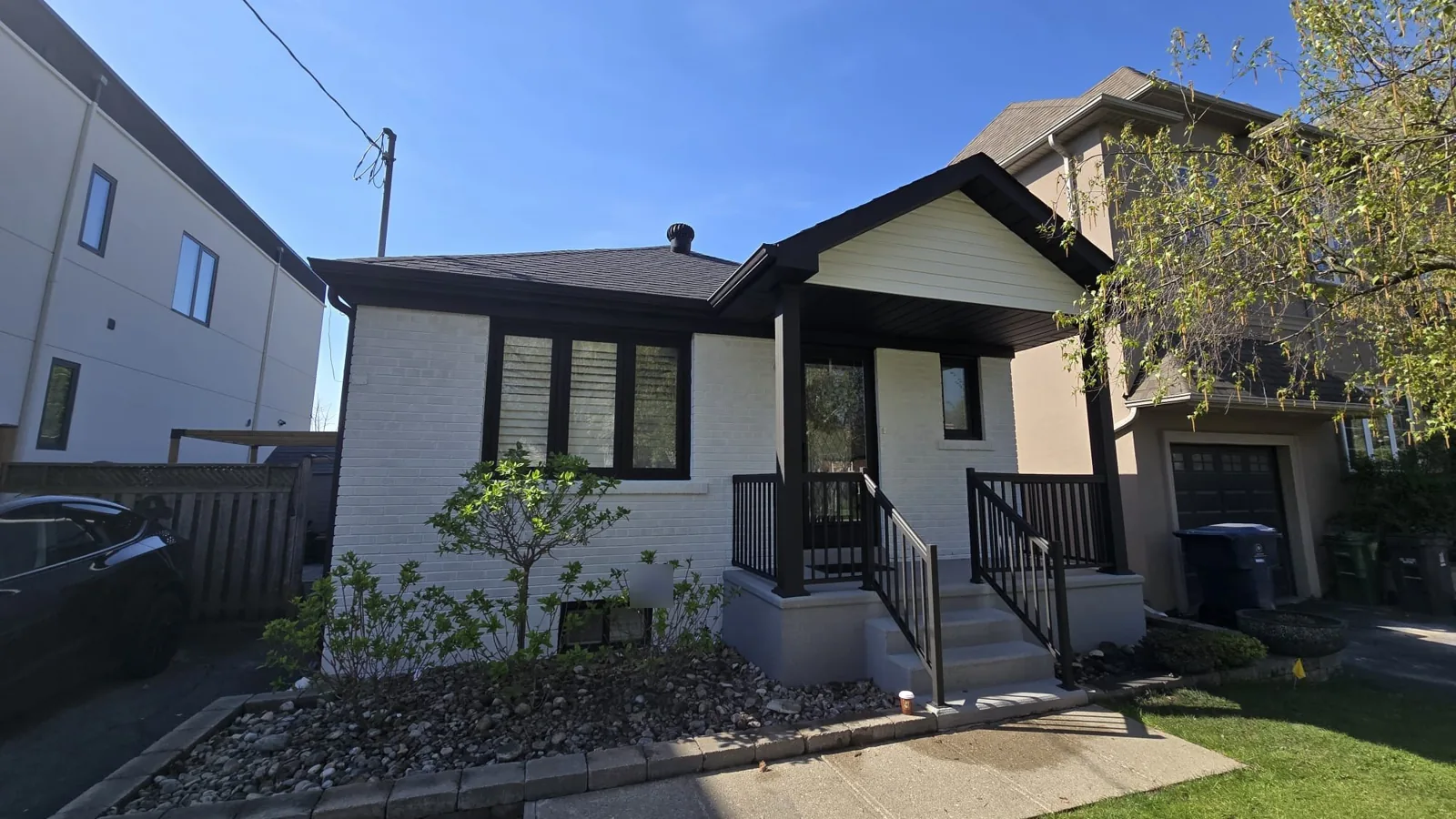 An Etobicoke bungalow after a full exterior repaint, with white painted brick and black windows, railings and trim