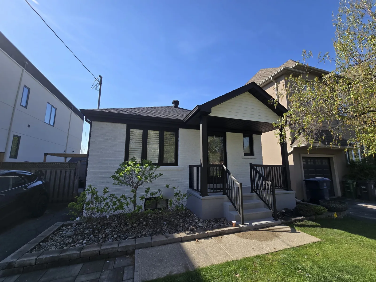 After: the bungalow with white painted brick and black windows, railings, gutters and porch trim