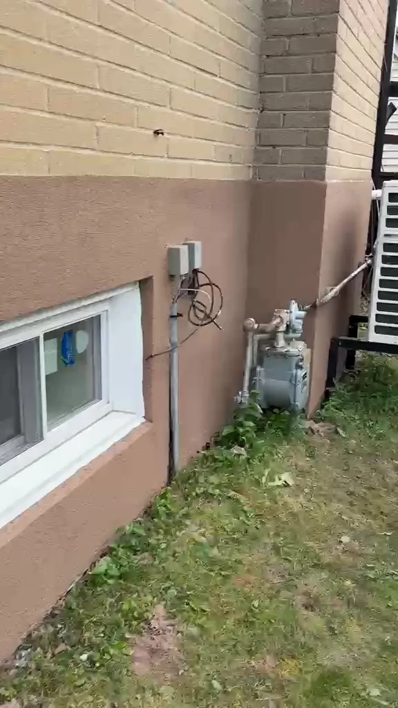 Finished side wall foundation in tinted stucco with the AC unit and a clean caulk line