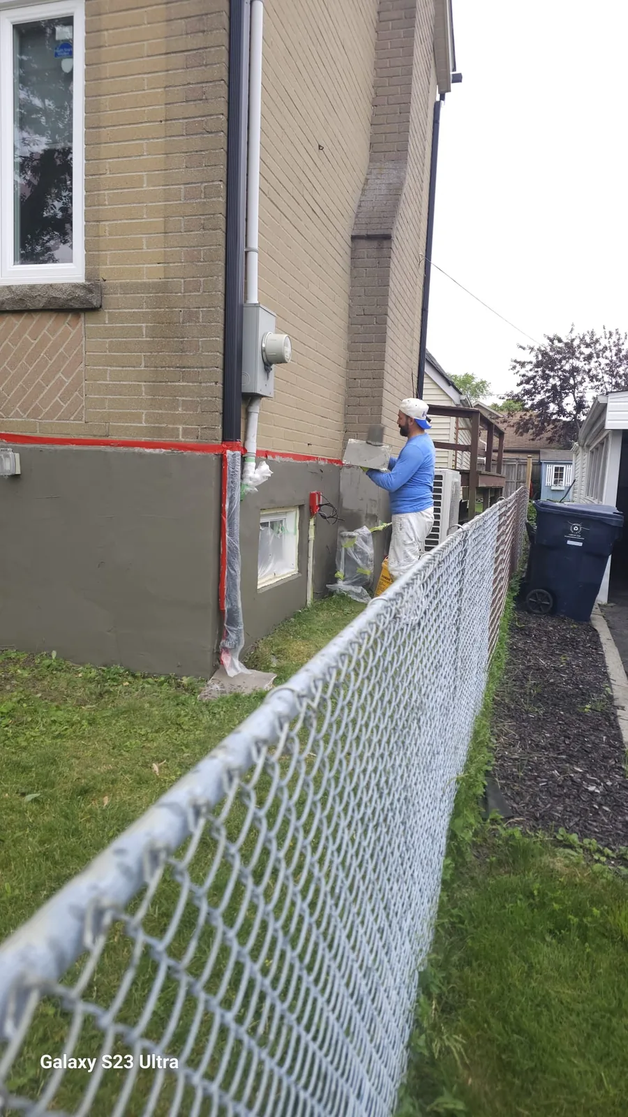 Base coat being worked around a masked basement window with the brick line taped off