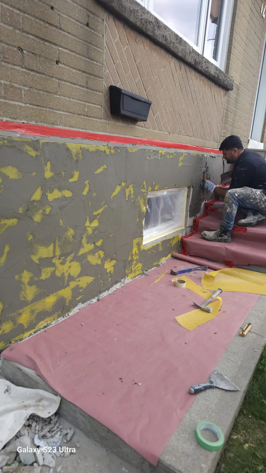 FAIME tradesperson hand-troweling the grey cementitious base coat onto the foundation