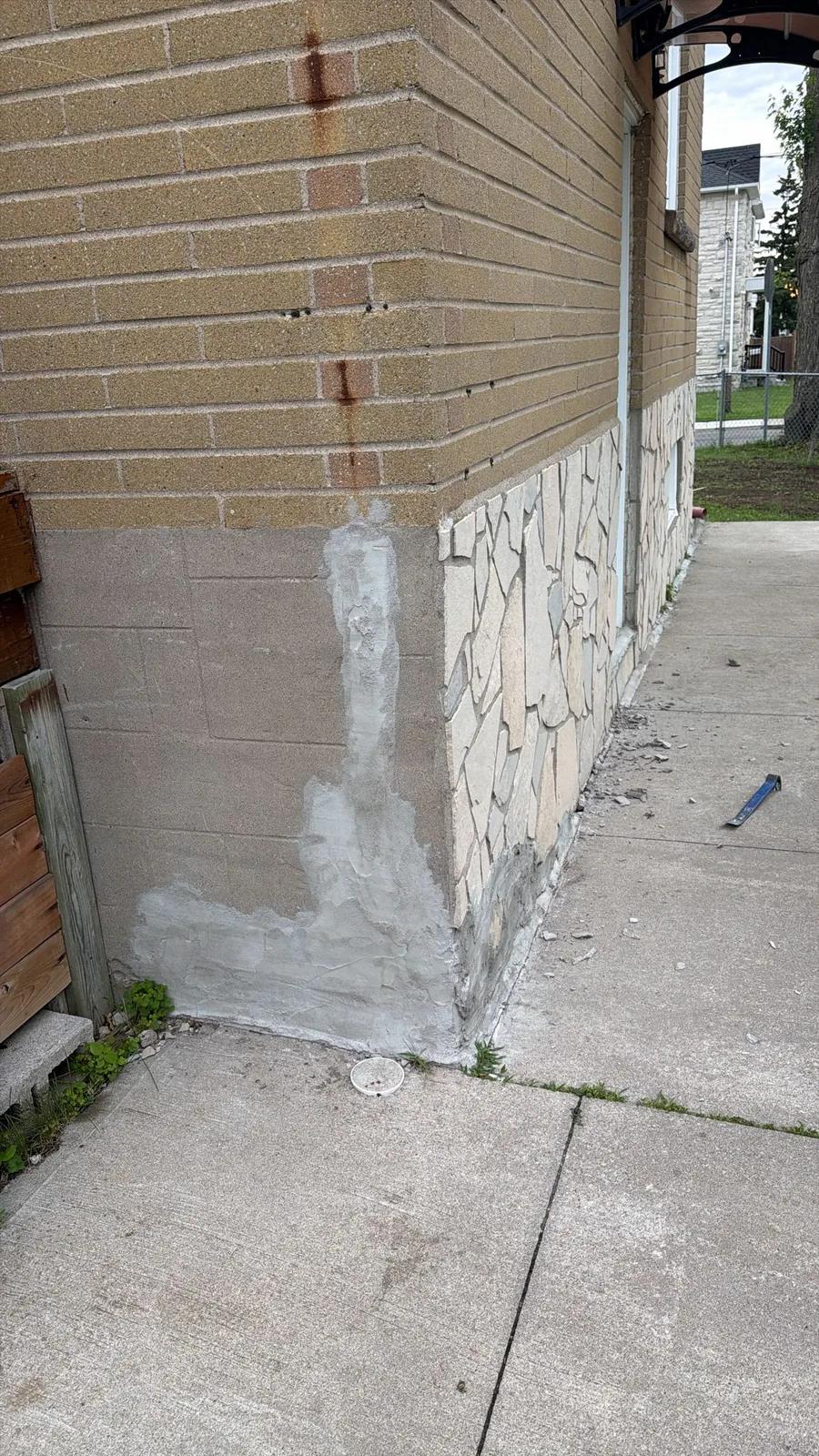 Failing parging and crack repair behind the old stone veneer at the corner