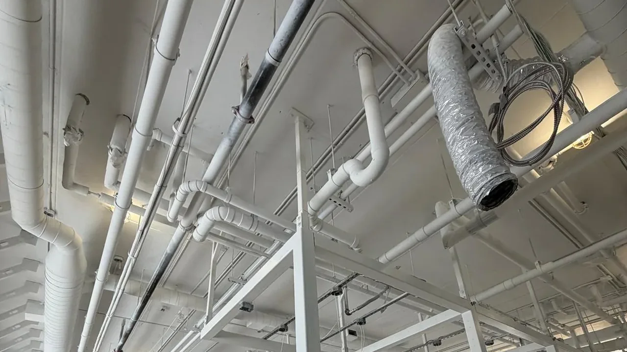 Ductwork, sprinkler piping and structural steel sprayed white across an open floor of a Kitchener supportive housing building painted by FAIME Construction