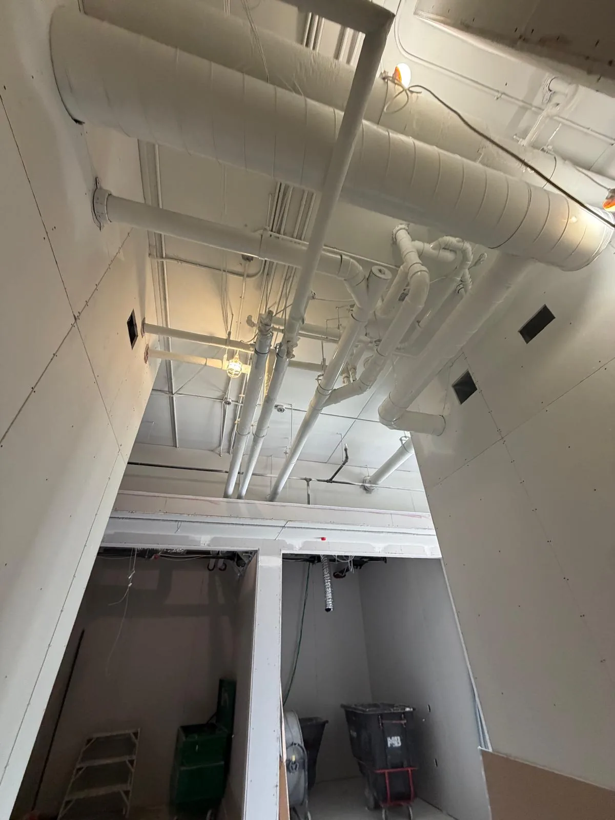Overhead ductwork and clustered piping finished white above drywall bulkheads