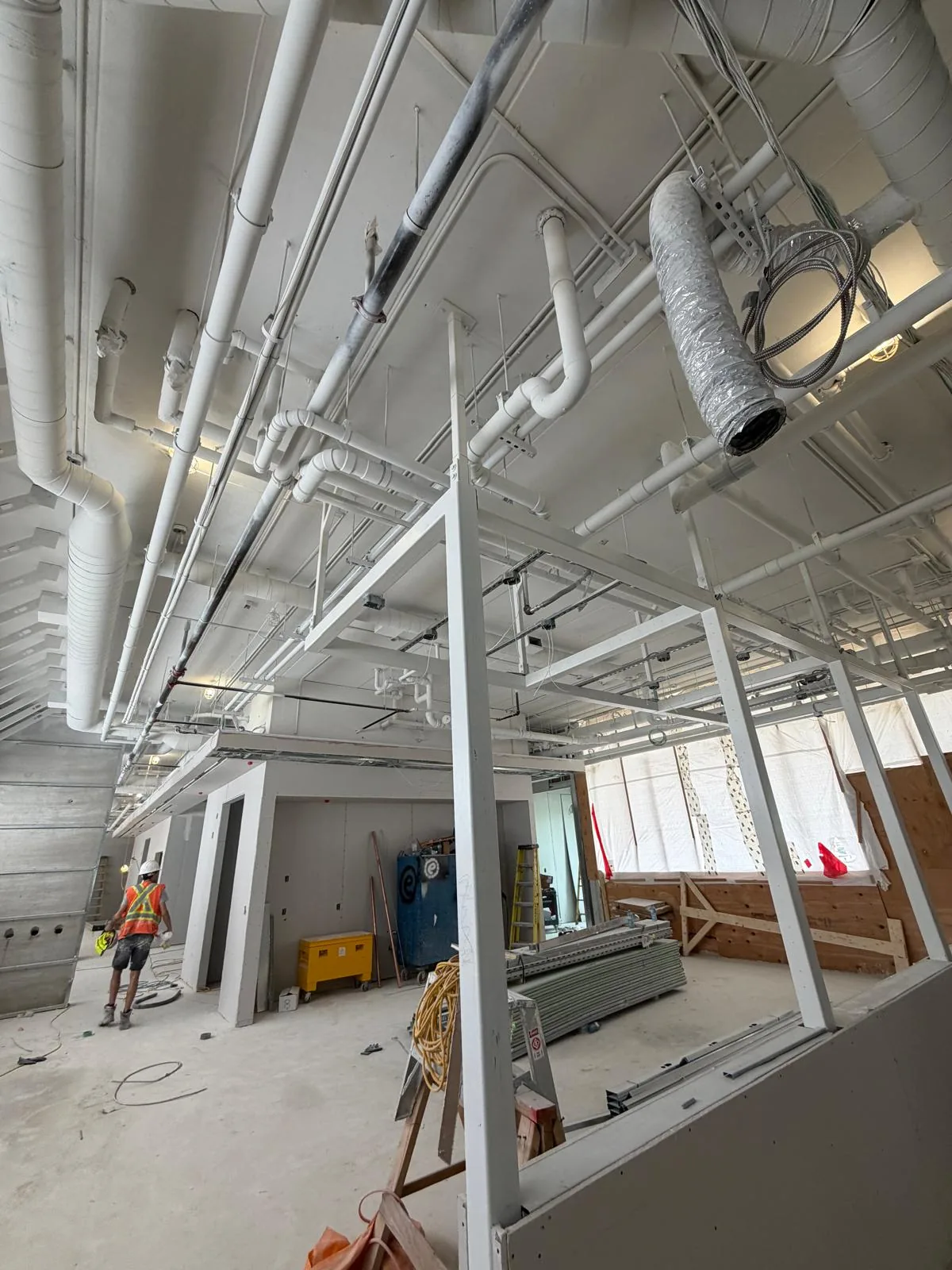 Open floor plate with ductwork, sprinkler piping, conduit and structural steel all sprayed white, a FAIME worker at the far wall