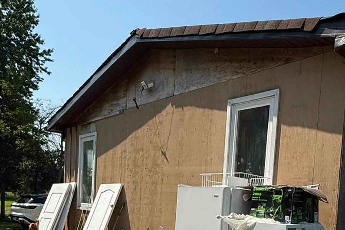 The same gable end stripped back to bare sheathing with removed material stacked against the wall