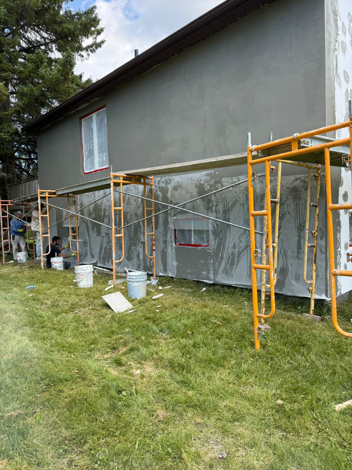 Scaffold set along the base-coated wall with the windows fully sheeted and masked before the finish coat