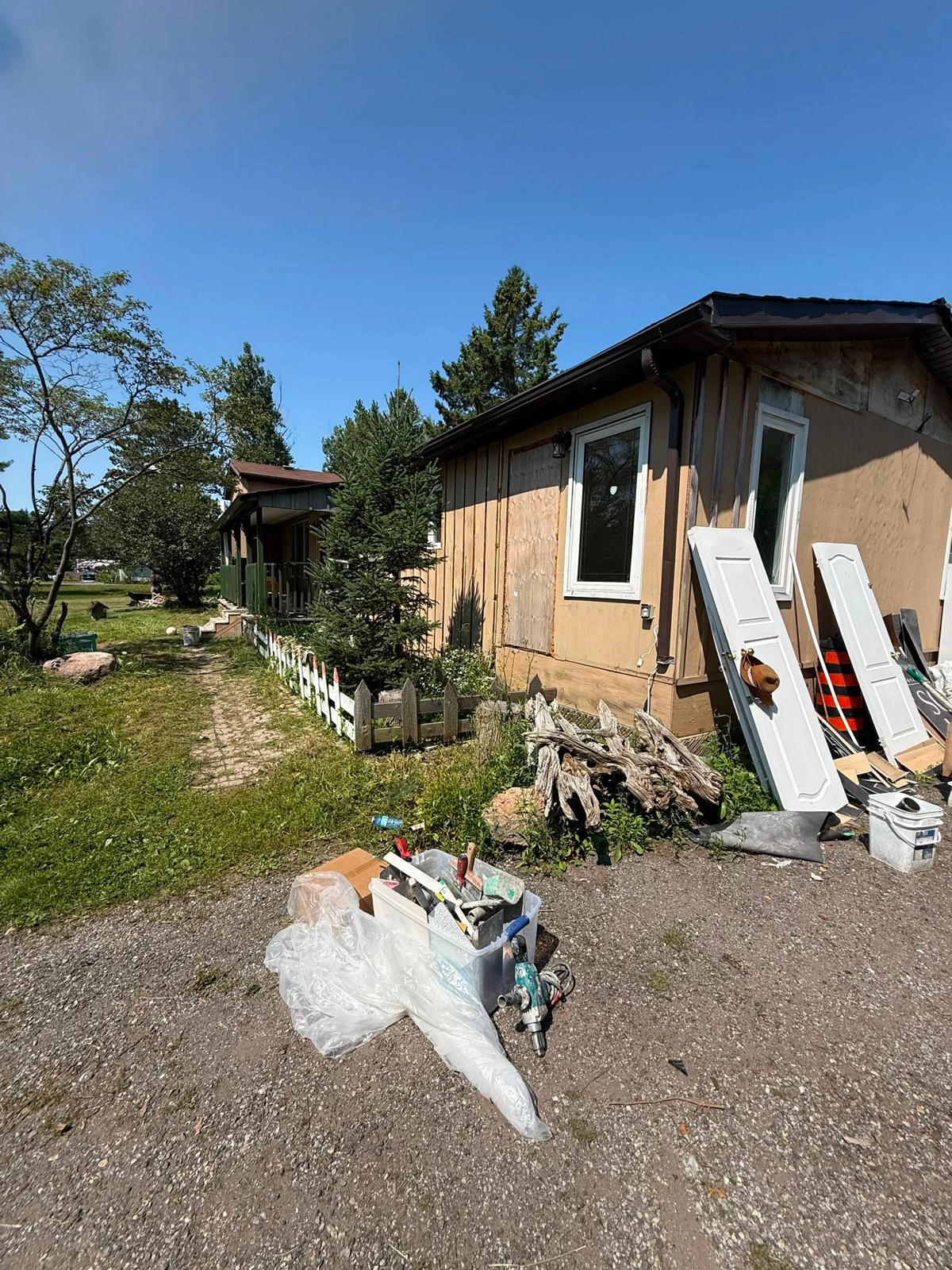 Side of the bungalow with the old exterior removed and doors and materials staged on the driveway