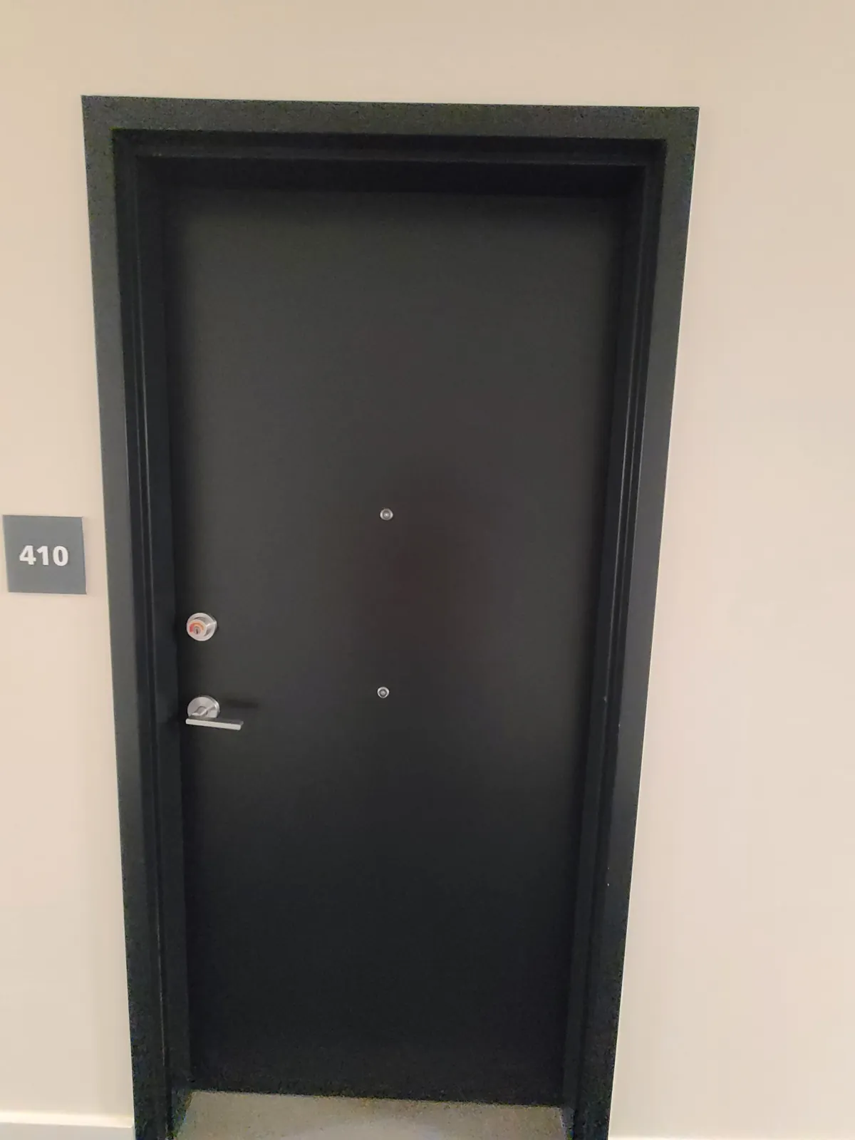 A suite entrance door and frame finished in a dark colour against a painted corridor wall