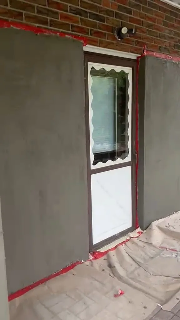 Fresh grey cementitious base coat around the rear door with the brick line taped in red