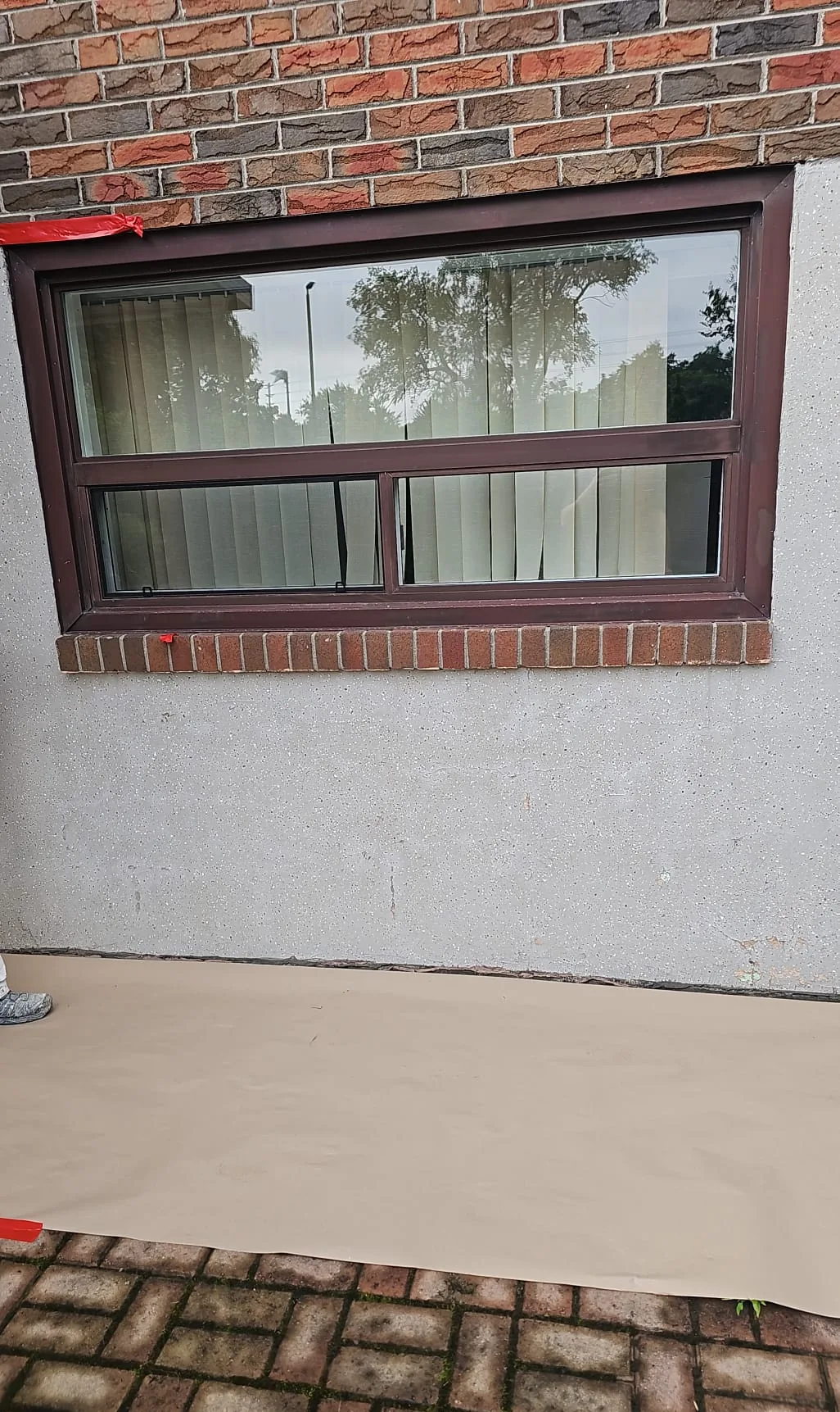 Old flaking coating around the masked basement window with drop paper laid down