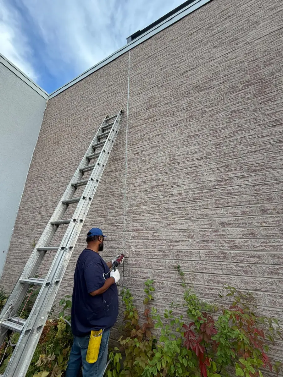 A FAIME tradesman on a ladder sealing the vertical control joint in a brick wall