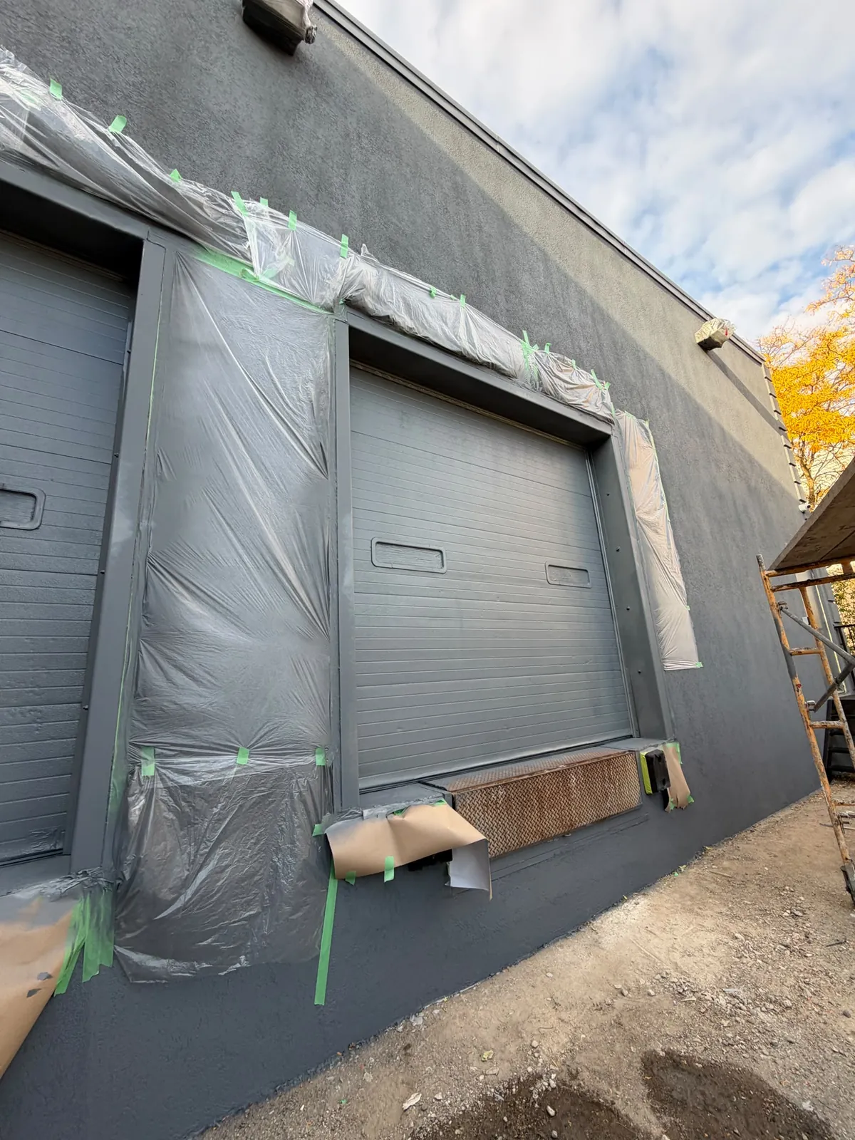 Two loading-dock doors sheeted in plastic and taped while the wall around them is painted