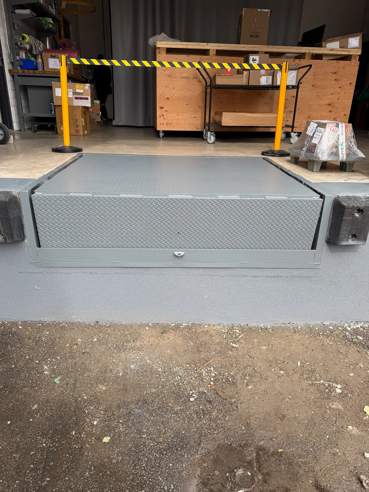 A second loading-dock leveler painted grey, with its steel edge and the wall below finished