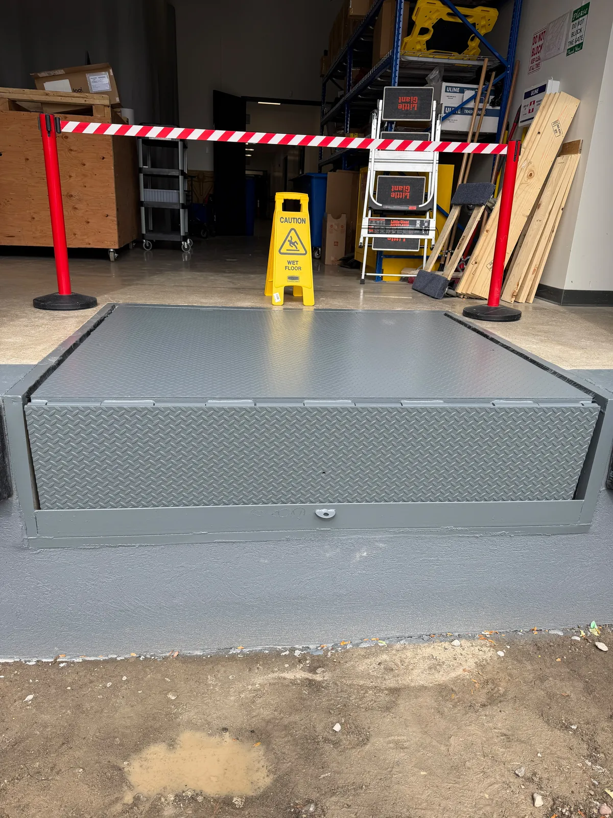 A loading-dock leveler and its steel frame painted grey, with the warehouse taped off behind