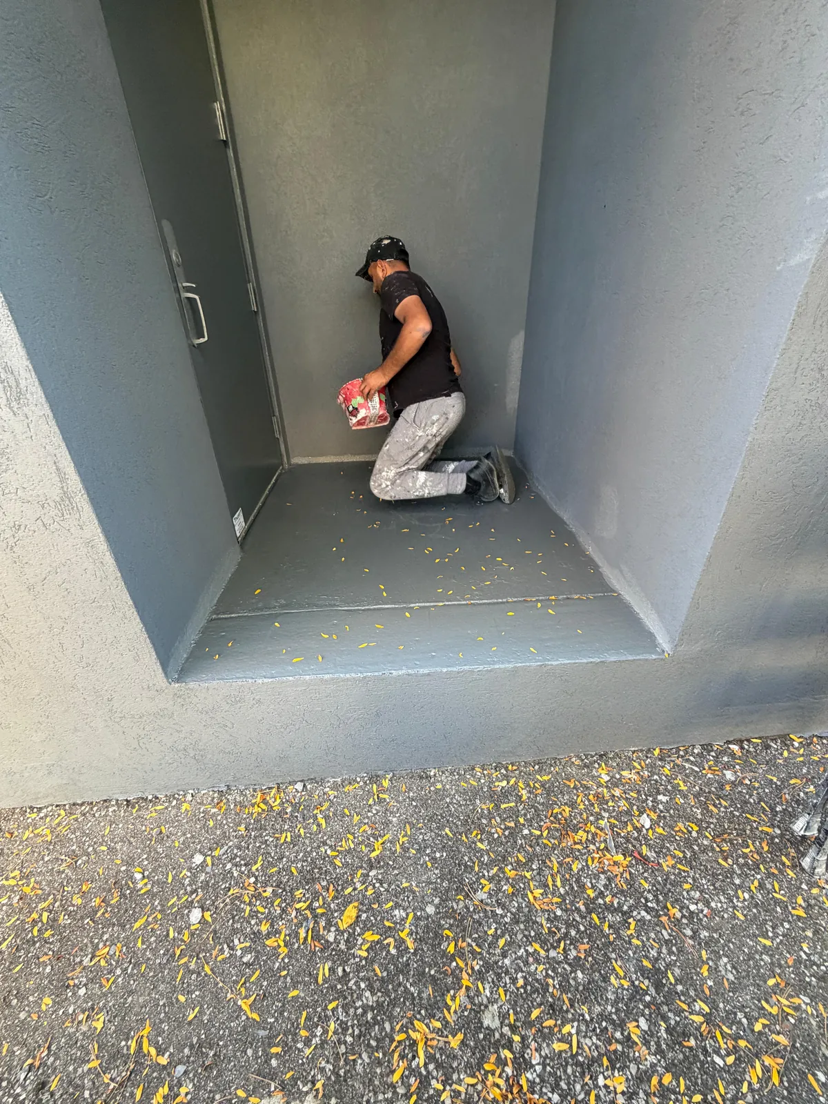 A FAIME painter kneeling inside a recessed service-door alcove, painting the walls