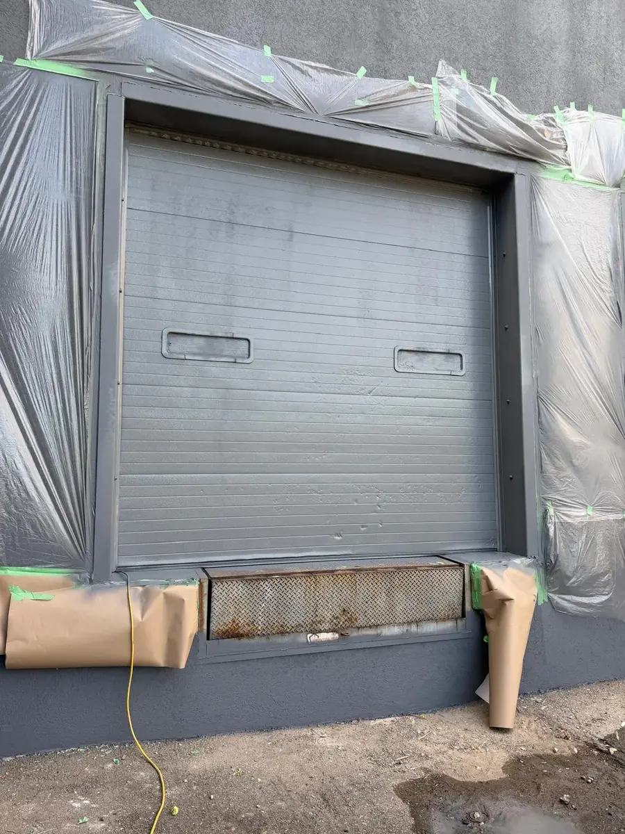 A loading-dock door fully wrapped in plastic sheeting and taped off before any coating work