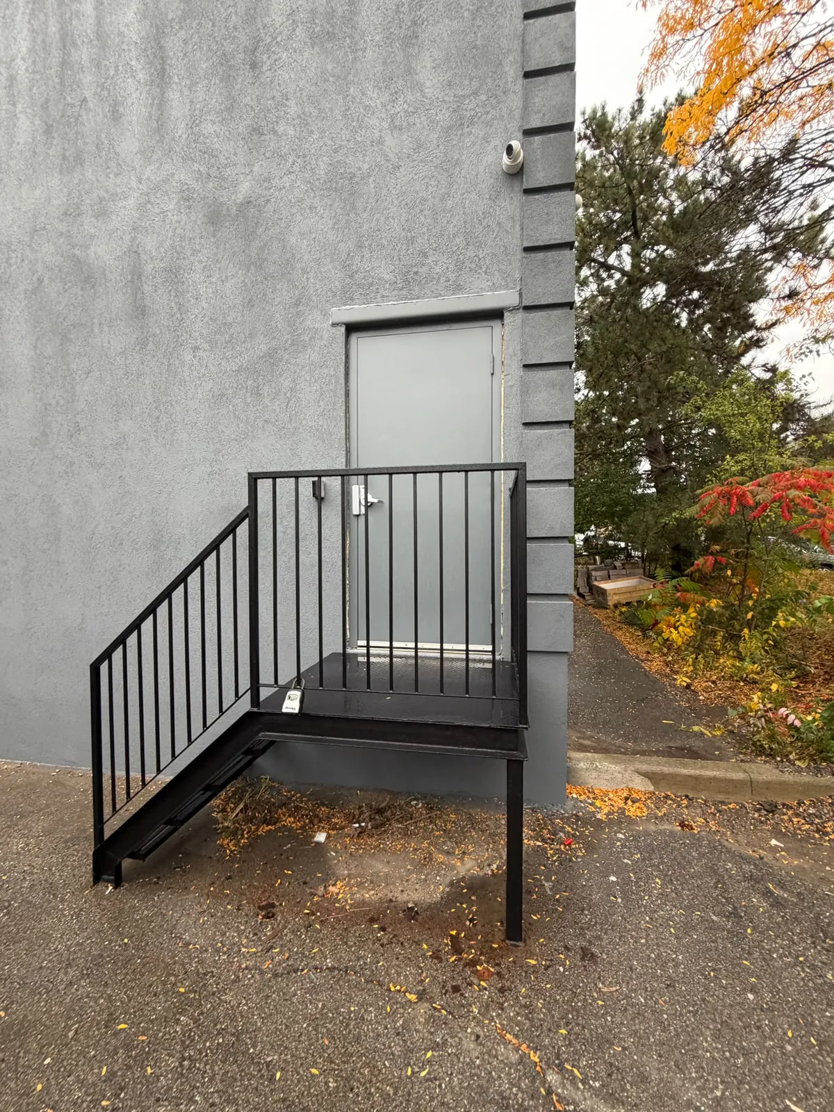 A painted black steel stair and railing leading to a rear service door on the grey wall