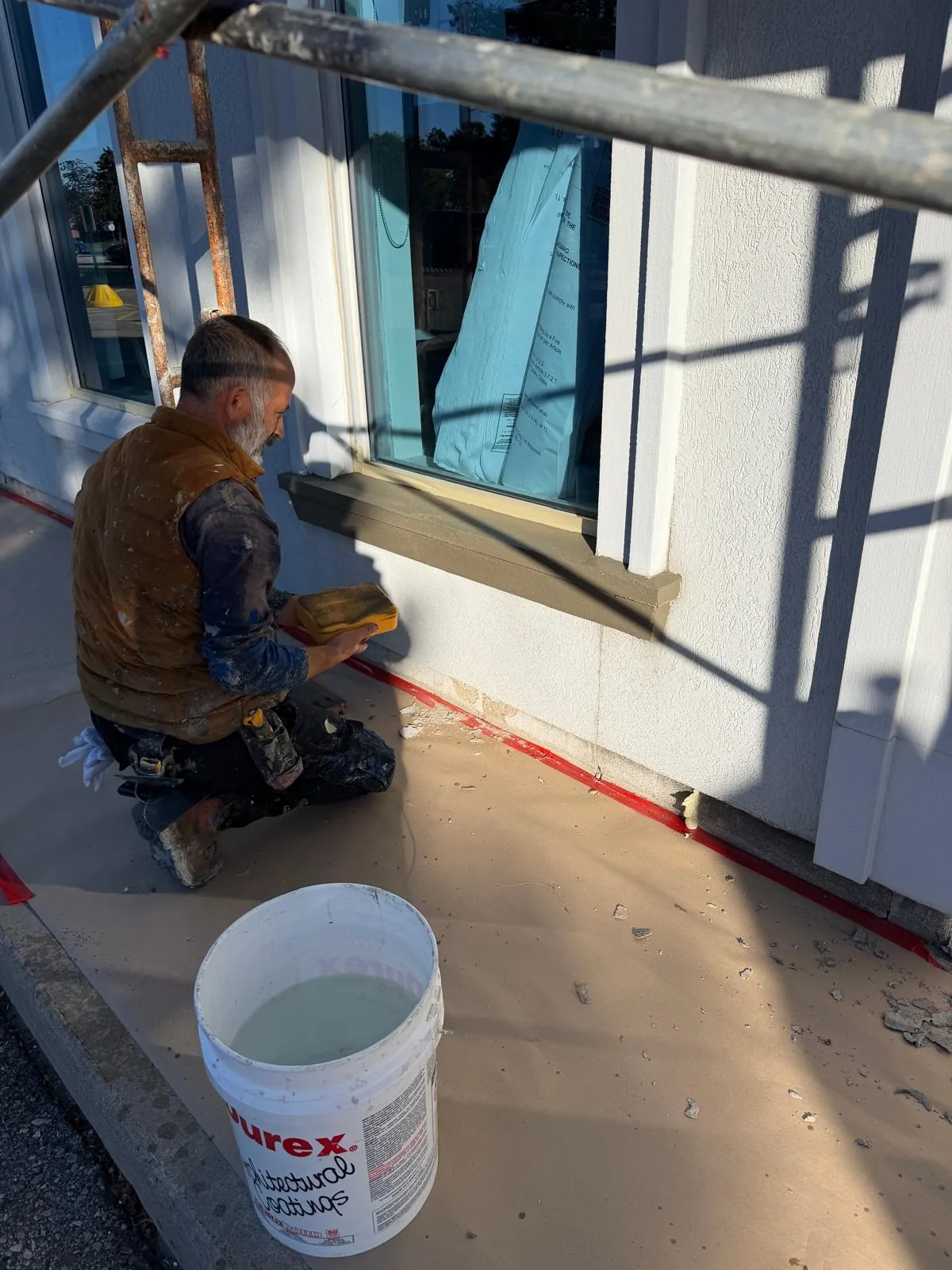 A FAIME tradesman kneeling at a window sill, finishing the new sill and caulking line