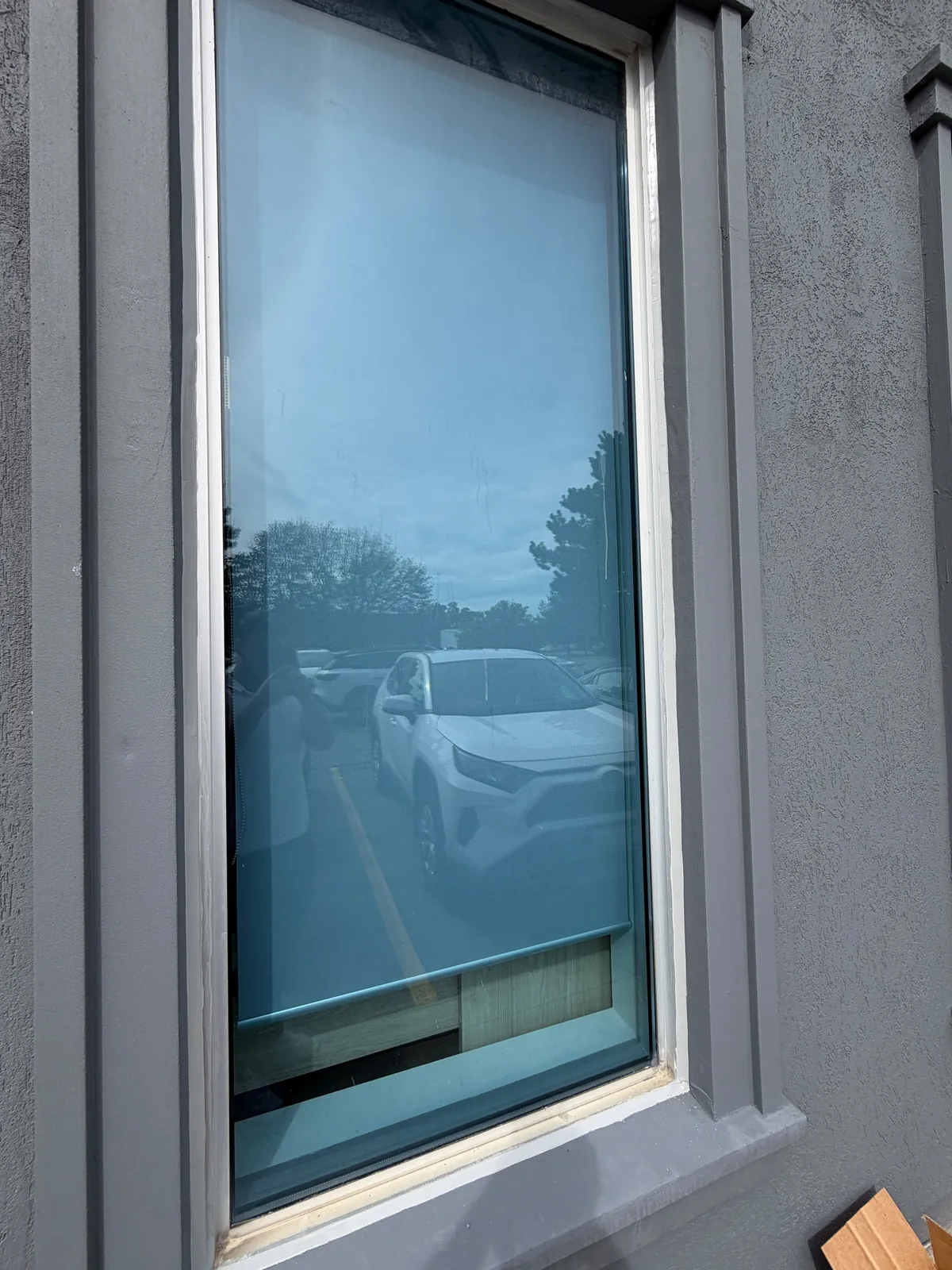A window with its new caulking and painted trim surround on the grey stucco wall