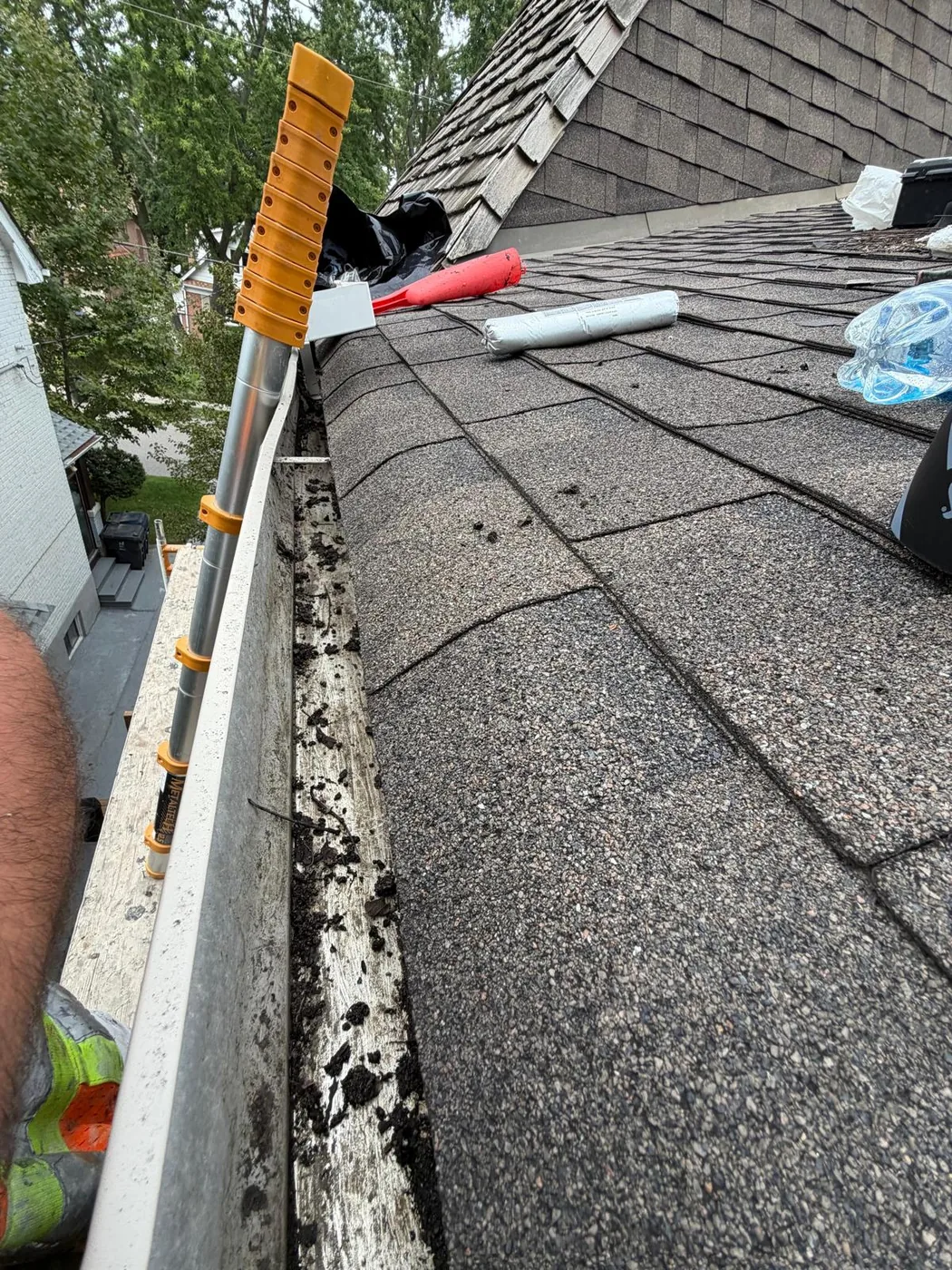 The same gutter line cleared out and running clean, with a ladder set against the fascia.