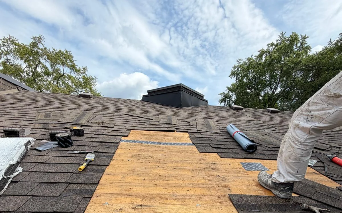 A Willowdale roof opened up during a leak repair, with shingles cut back around a new plywood deck section and a FAIME crew member working alongside it