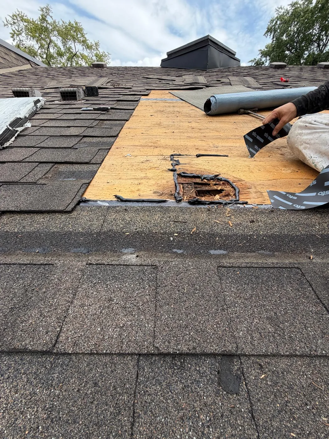 A rotted opening in the roof deck with splintered edges, with Sto tape being rolled down over the repaired area.