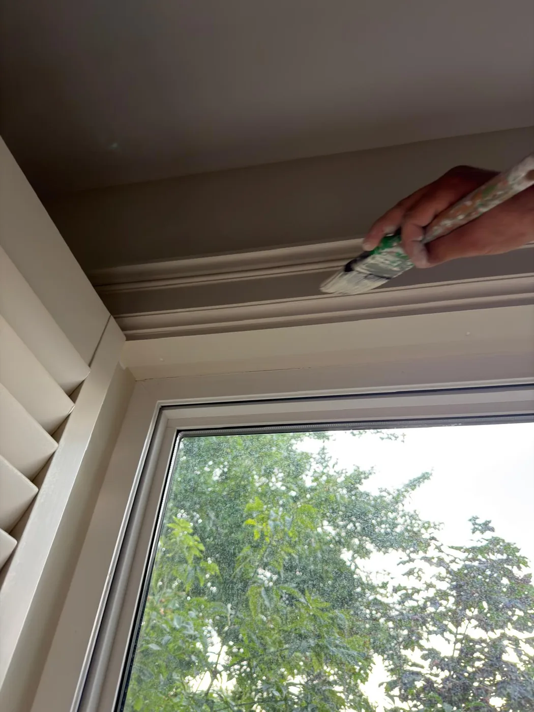 A brush cutting in fresh paint along the head casing of an upstairs window.