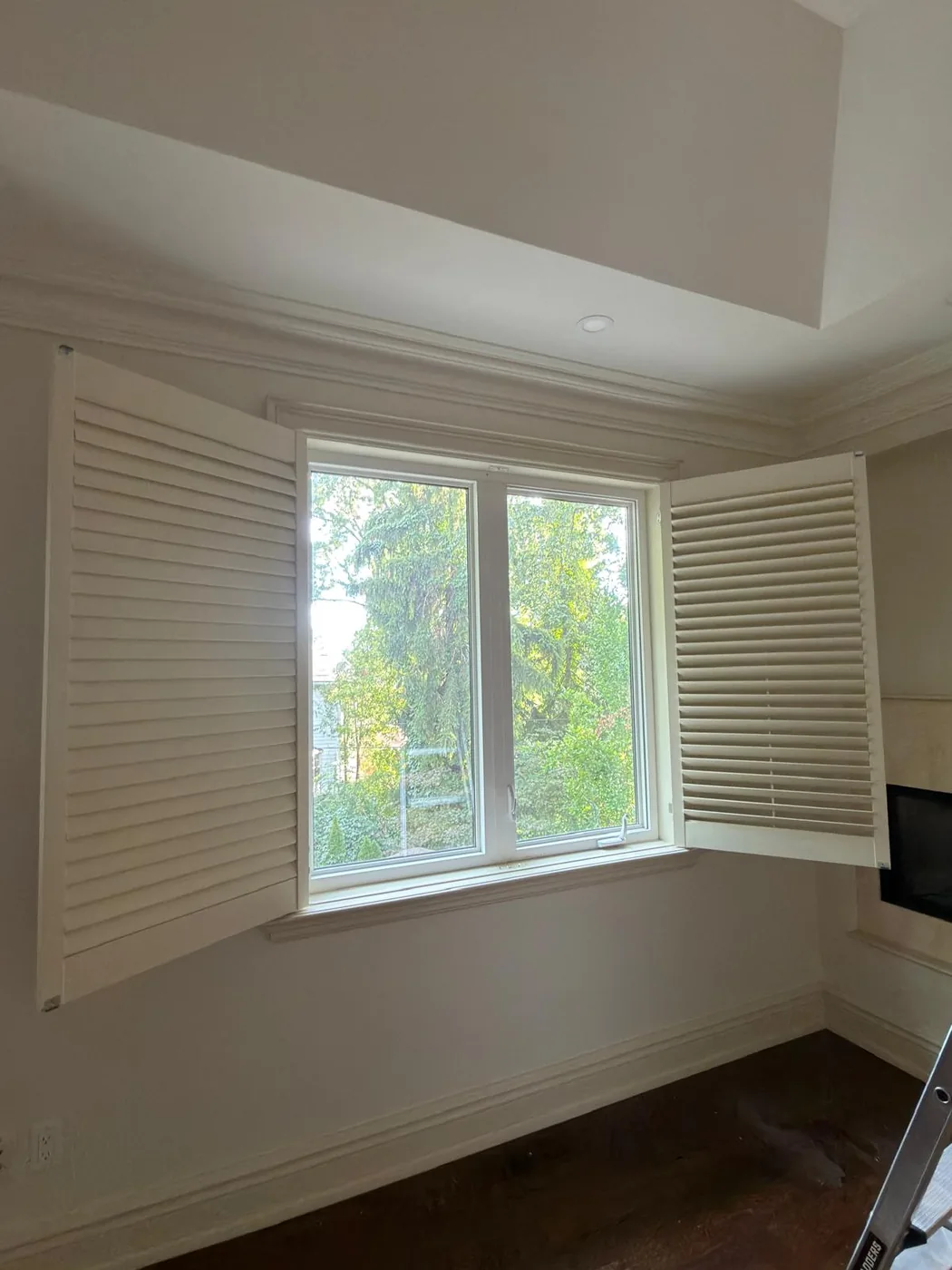 A finished upstairs window flanked by white plantation shutters after refinishing.
