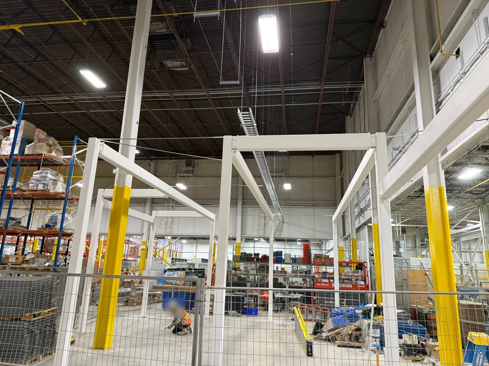 Coated frames inside a fenced work area, with warehouse racking beyond