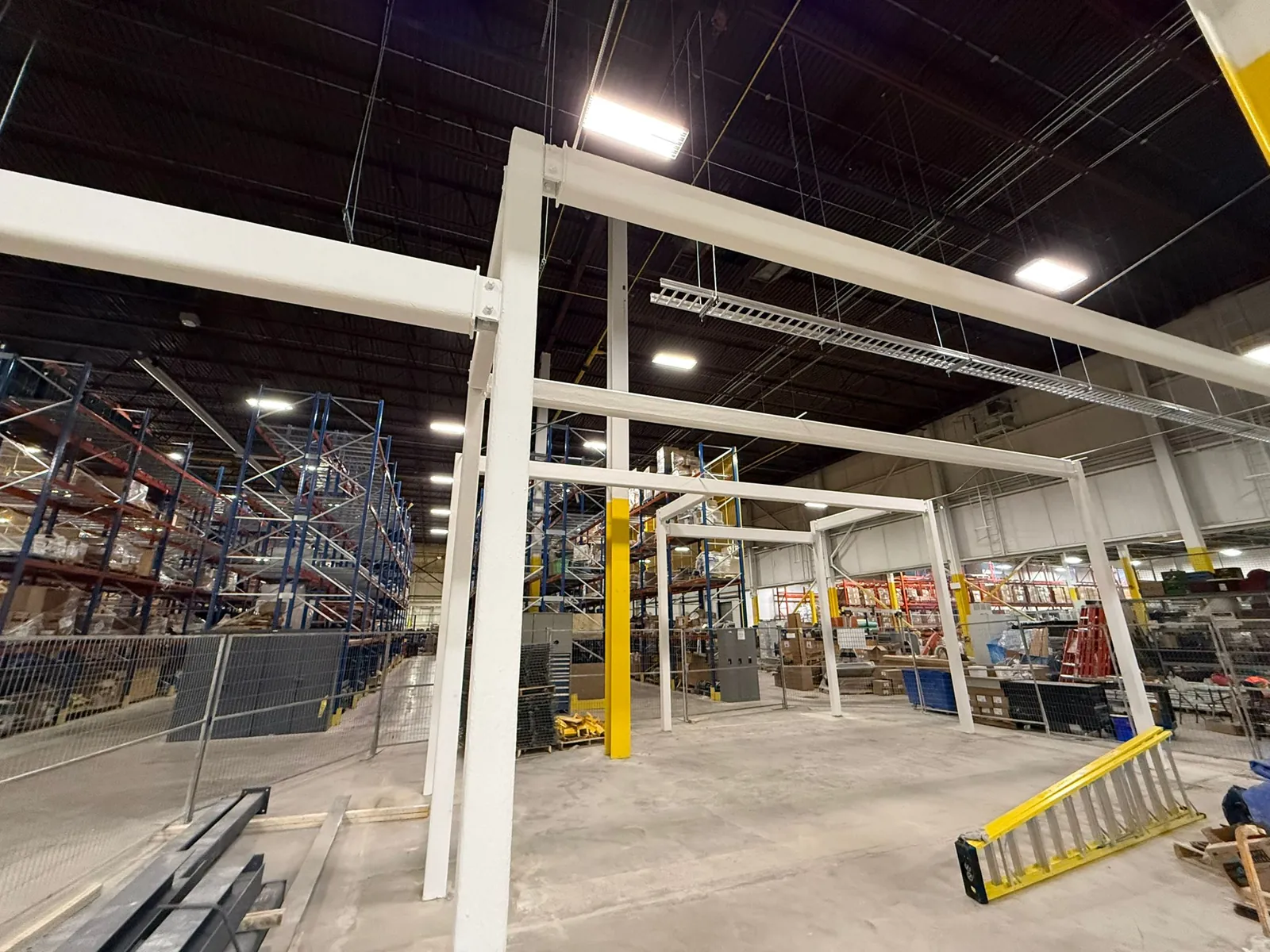 A run of steel frames coated in white intumescent fireproofing across the warehouse floor